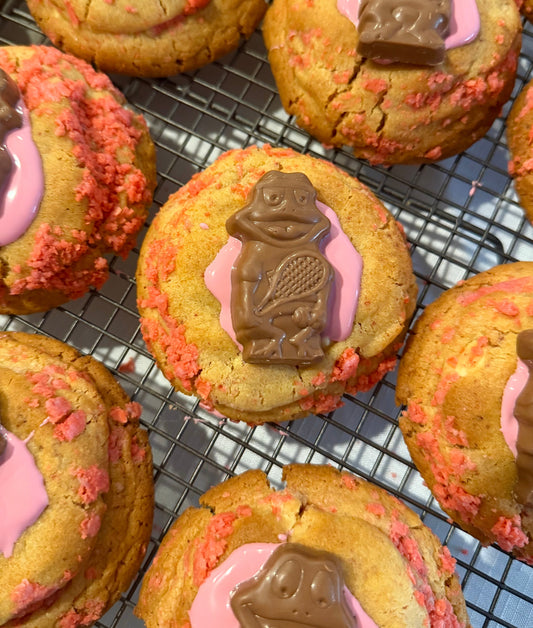 Freshly baked cookies with pink icing and chocolate frog decorations on cooling rack from Bake With Mimi